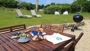 A wooden table with a picnic setup including a loaf of bread, blue mugs, a bag of chips, and a t-shirt.