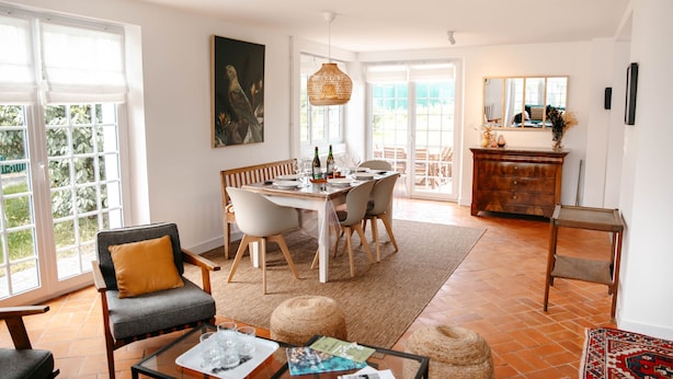 A dining area with a table set for four, surrounded by chairs, a sofa, and a coffee table with magazines.