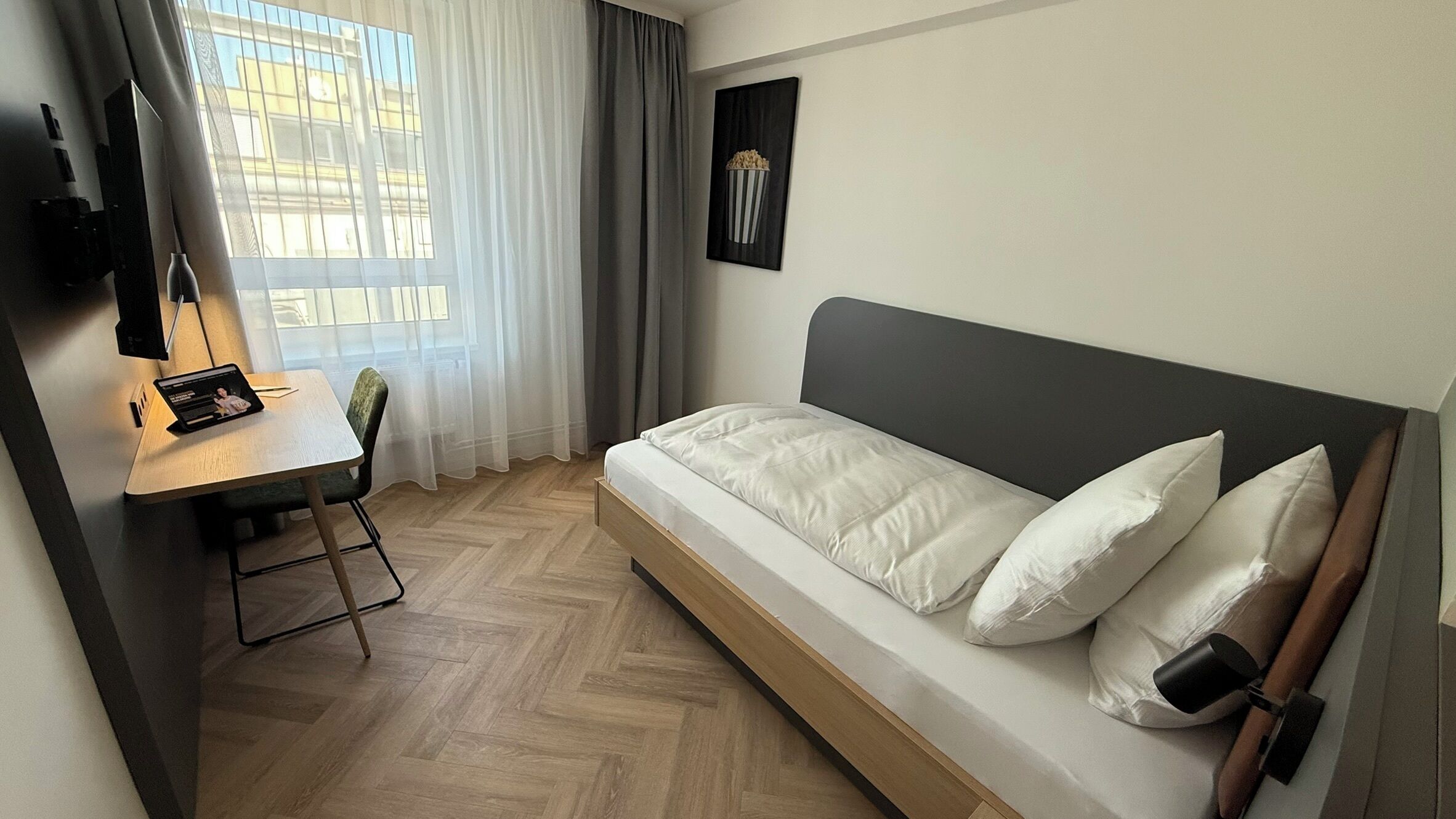 Habitación de hotel con cama, escritorio, silla, televisor y ventana con cortinas.