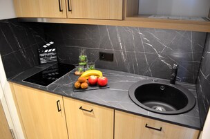 A kitchen with a black marble countertop, a black sink, and wooden cabinets.