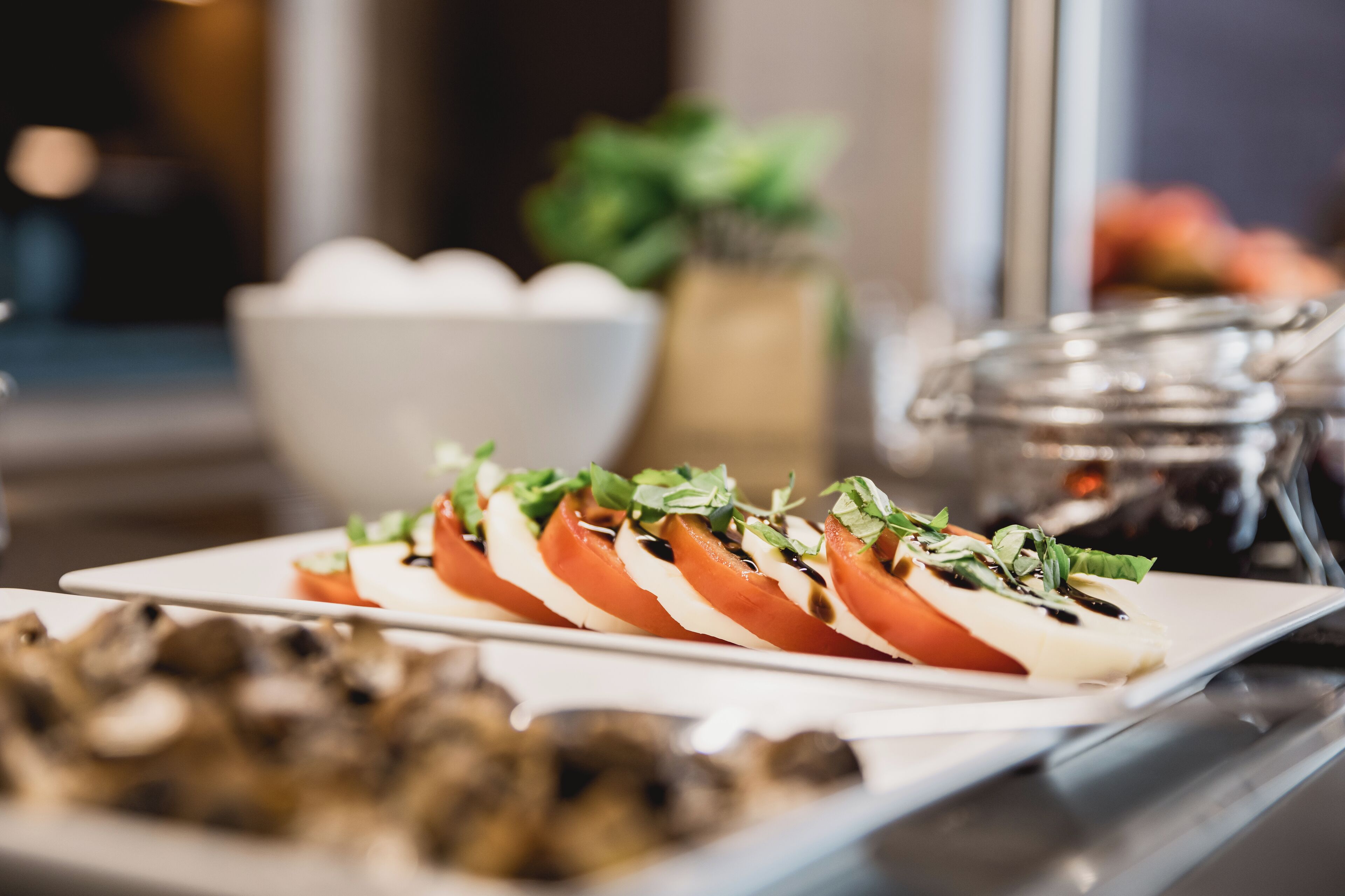 Une assiette de salade caprese, composée de tomates, de mozzarella et de basilic, sur fond flou représentant une cuisine.