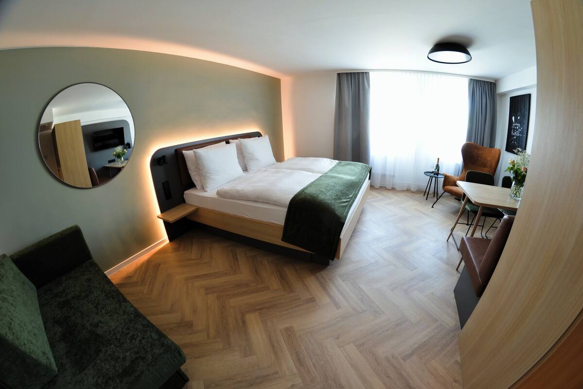 Une chambre d’hôtel avec un lit, un bureau, une chaise, un miroir et une vue sur la ville.