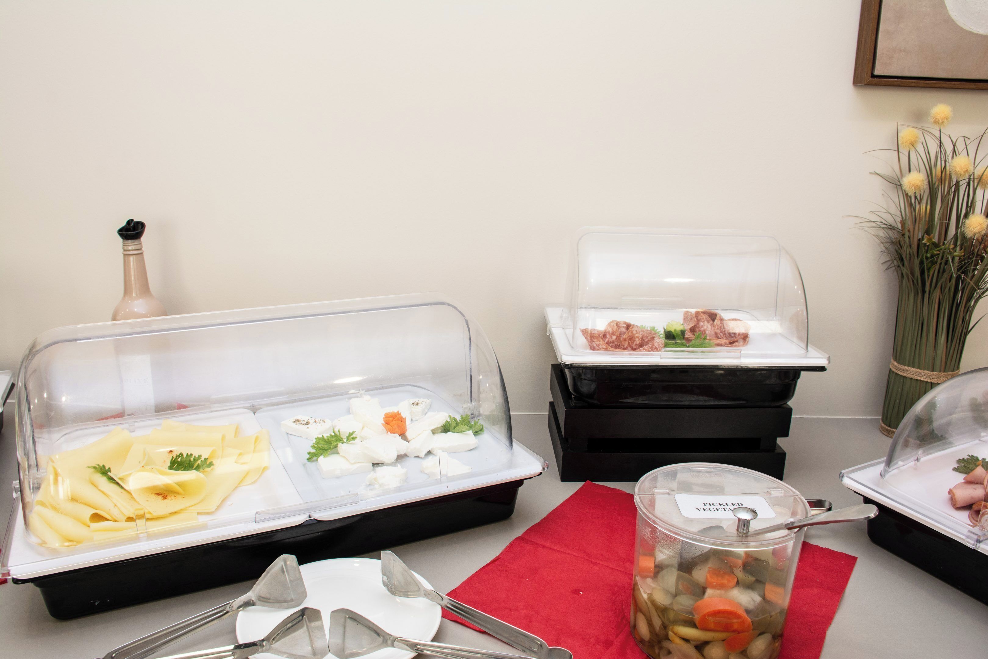 Montaje de bufé con recipientes para alimentos cubiertos, utensilios de servicio y un jarrón decorativo.
