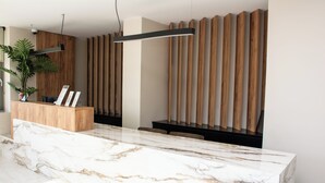 Un espace d’accueil doté d’un comptoir en marbre, d’un bureau d’accueil en bois, d’une plante en pot et de lambris en bois verticaux sur le mur.