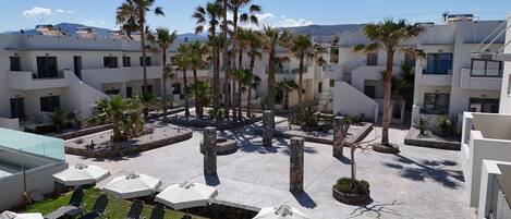 A courtyard with lounge chairs and umbrellas, surrounded by palm trees and modern buildings.