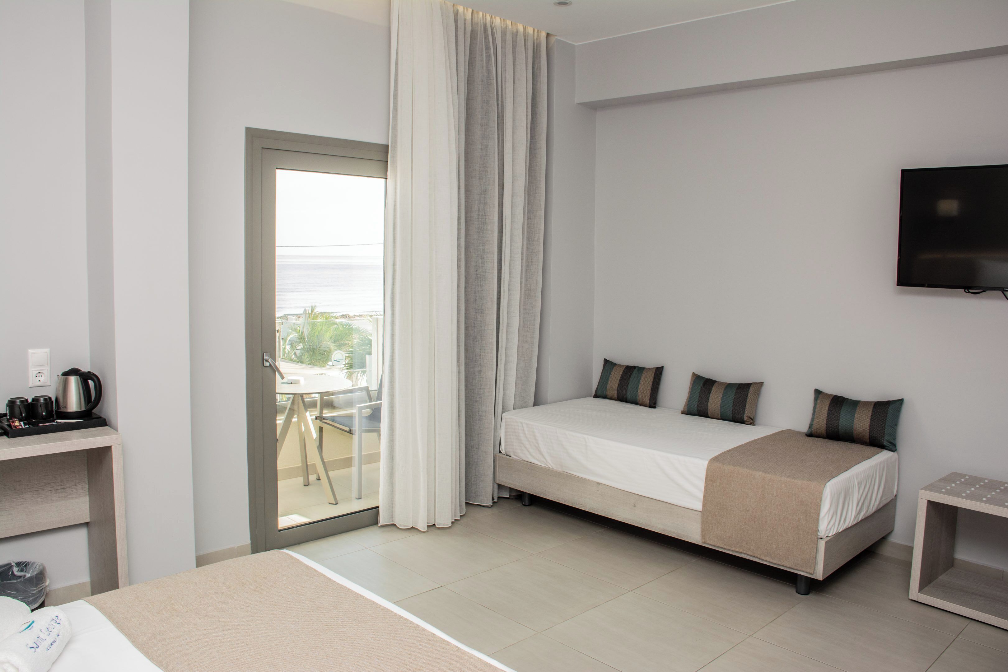 A hotel room with a bed, a TV, a desk with a coffee maker, and a view of the outdoors.