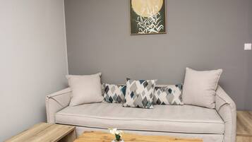 A neutral-toned sofa with patterned pillows, a wooden coffee table with a vase of flowers, and a wall-mounted artwork.