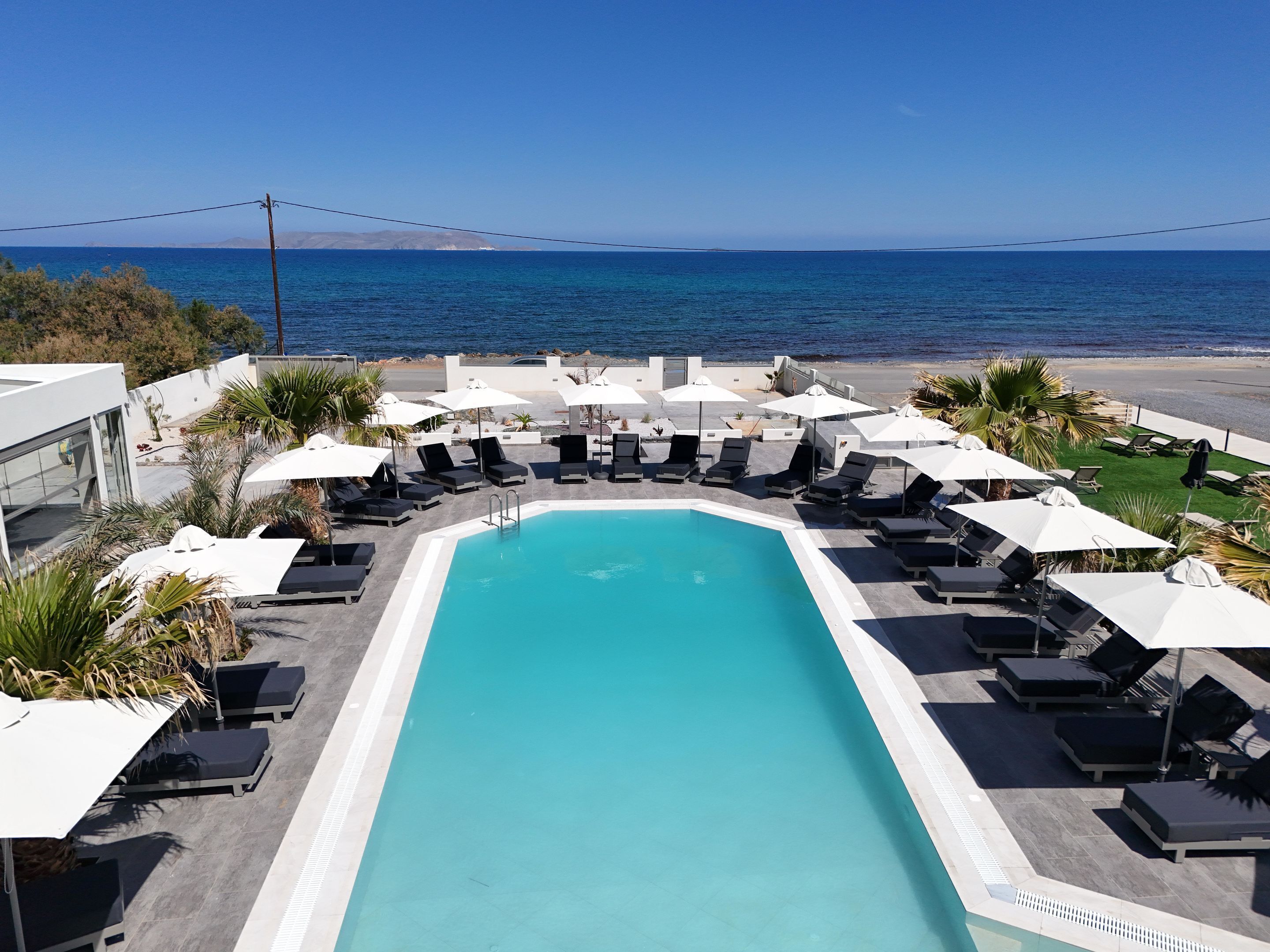 A pool area with lounge chairs and umbrellas, overlooking a beach and the ocean.