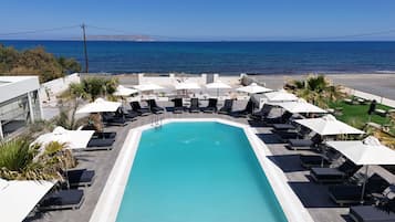 A pool area with lounge chairs and umbrellas, overlooking a beach and the ocean.