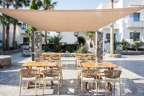 Een terras buiten met tafels en stoelen, omringd door stenen muren en palmbomen.
