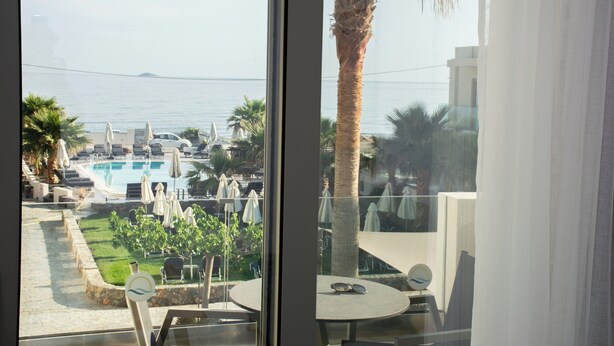 Un balcon offrant une vue sur une piscine, des palmiers et une île lointaine.