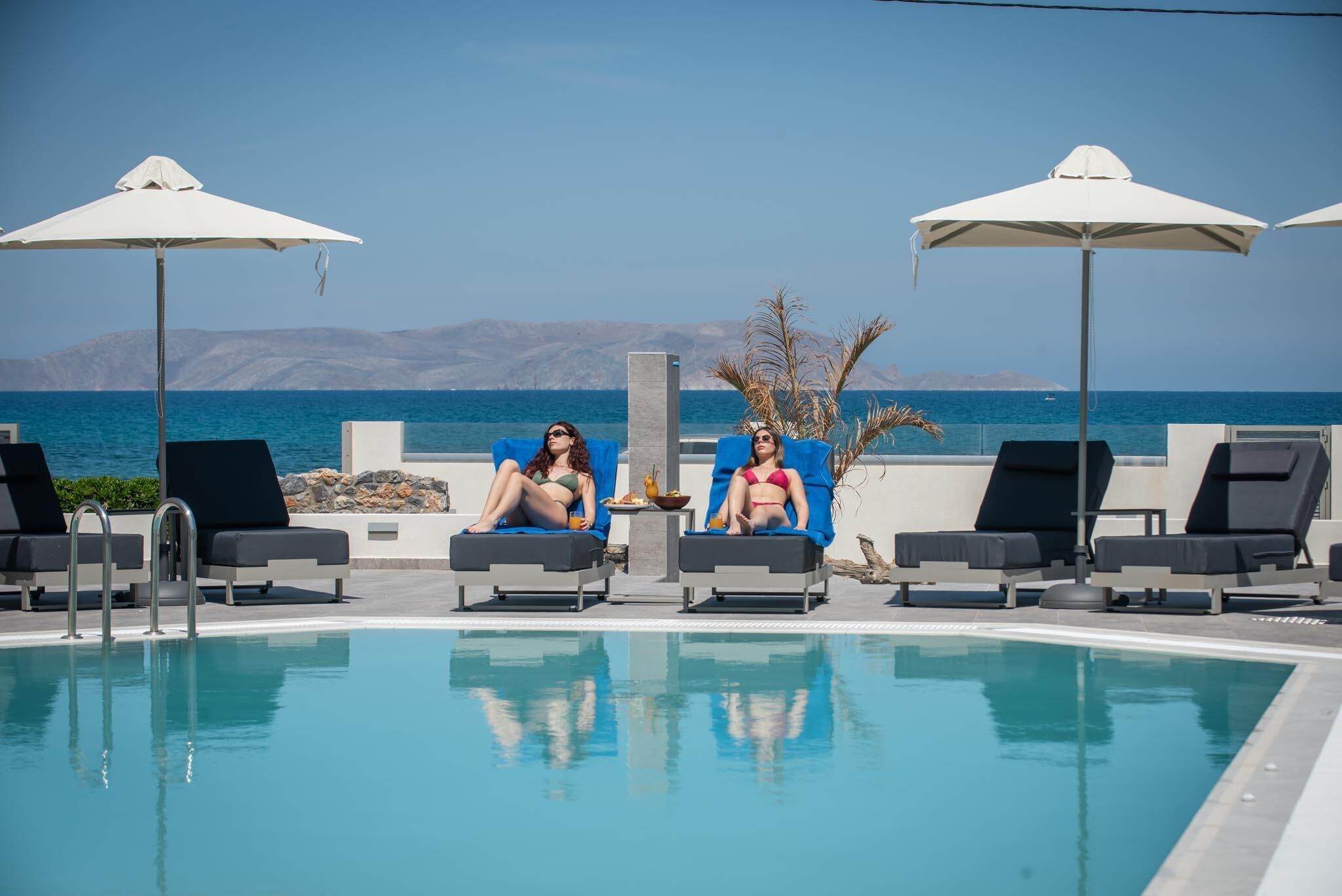 Zona junto a la piscina con sillones de descanso y sombrillas, vista despejada al mar y montañas al fondo.