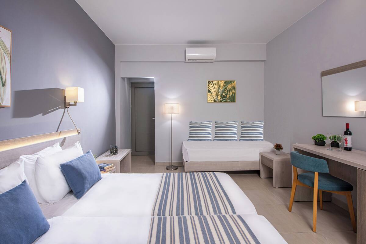 Une chambre d’hôtel moderne équipée de deux lits, d’un bureau, d’une chaise et d’une petite table agrémentée d’une plante et d’une bouteille.