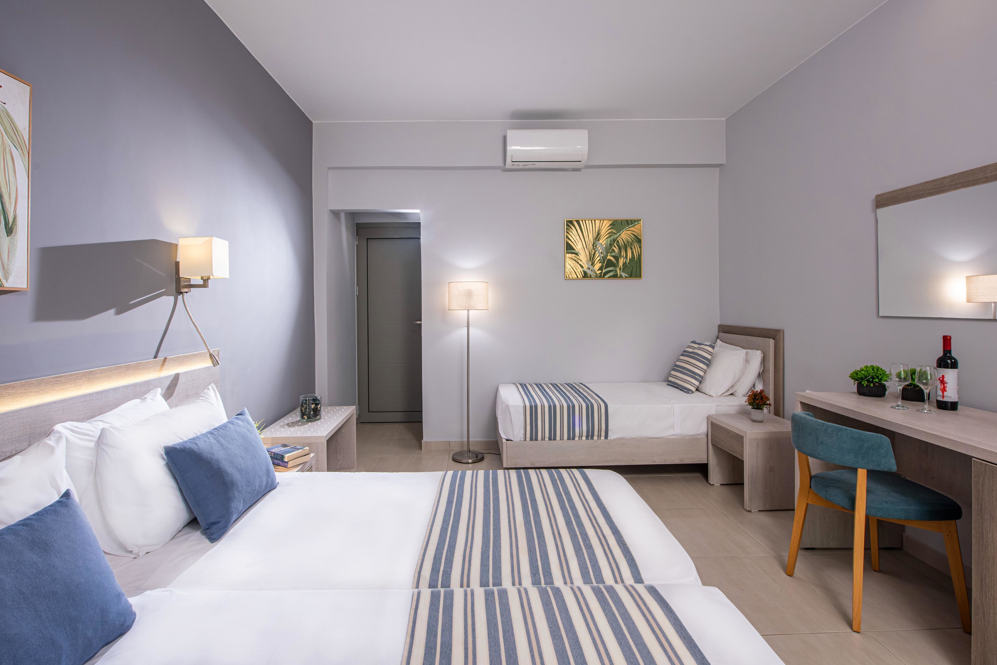 A modern hotel room with two beds, a desk, a chair, a desk lamp, a floor lamp, a small table with a plant, and a wall-mounted TV.