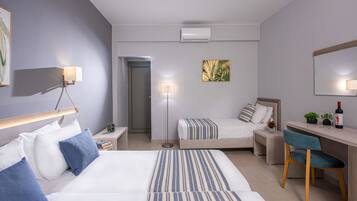Quarto de hotel moderno com duas camas, uma escrivaninha, uma cadeira, luminária de mesa, luminária de chão, uma mesinha com uma planta e uma TV fixada na parede.