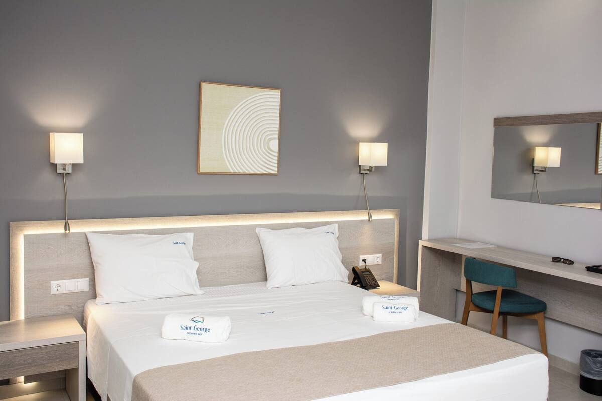Une chambre d’hôtel comprenant un lit, des tables de chevet, un bureau, une chaise, un miroir et une œuvre d’art accrochée au mur.