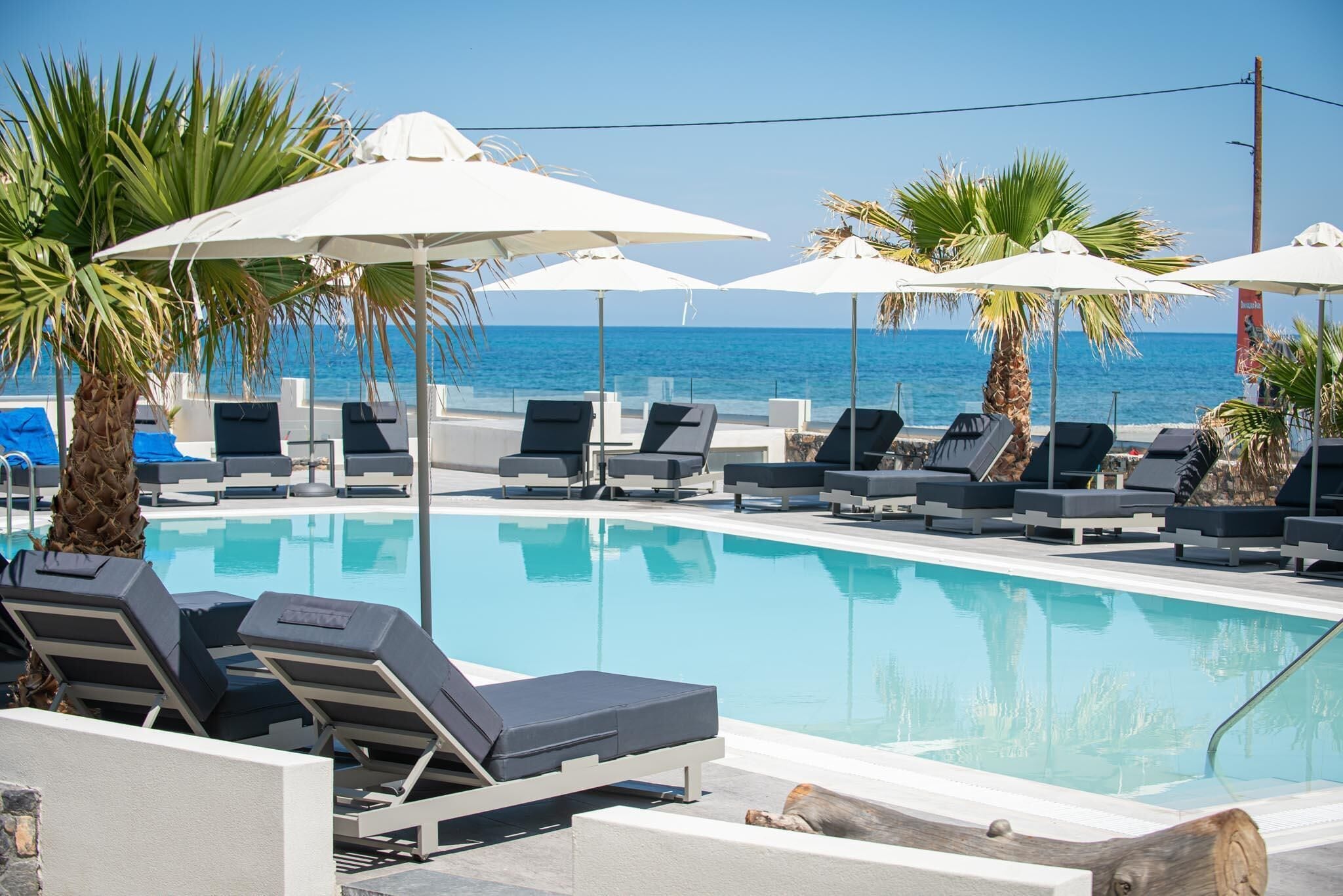 Zona junto a la piscina con sillones de descanso y sombrillas, vista despejada al mar y una piscina tranquila.
