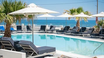 Zona junto a la piscina con sillones de descanso y sombrillas, vista despejada al mar y una piscina tranquila.