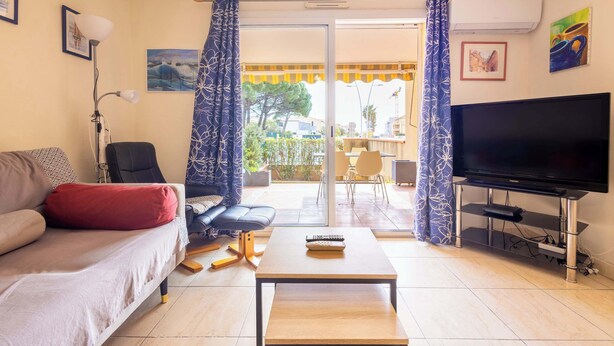 A living room with a sofa, a coffee table, a TV, and a sliding glass door leading to an outdoor area. - Beach and Comfort Your Stay Near the Sea (Valras-Plage)