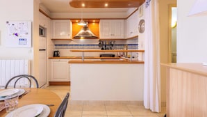 A kitchen with white cabinets, a wooden countertop, a hanging light fixture, and a clock on the wall. - Beach and Comfort Your Stay Near the Sea (Valras-Plage)