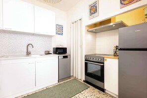 Una cocina compacta con armarios blancos, horno de acero inoxidable, microondas y refrigerador.