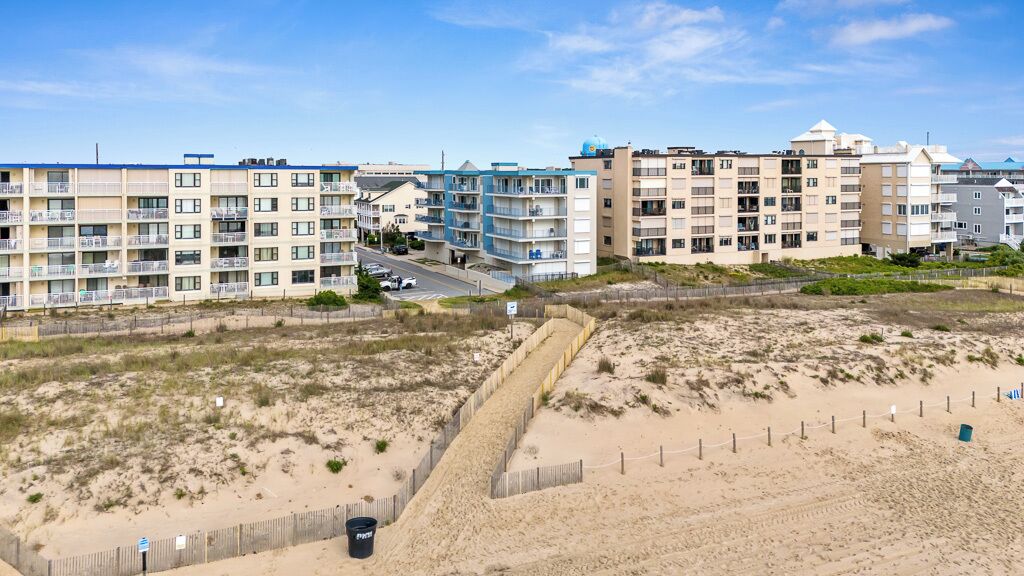 Un hotel frente a la playa con varios pisos, una playa arenosa y un cielo despejado.