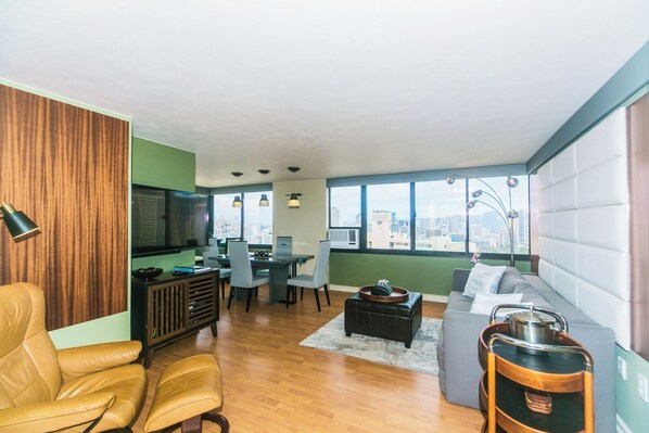 A modern living room with a sofa, chairs, a dining table, and a television.
