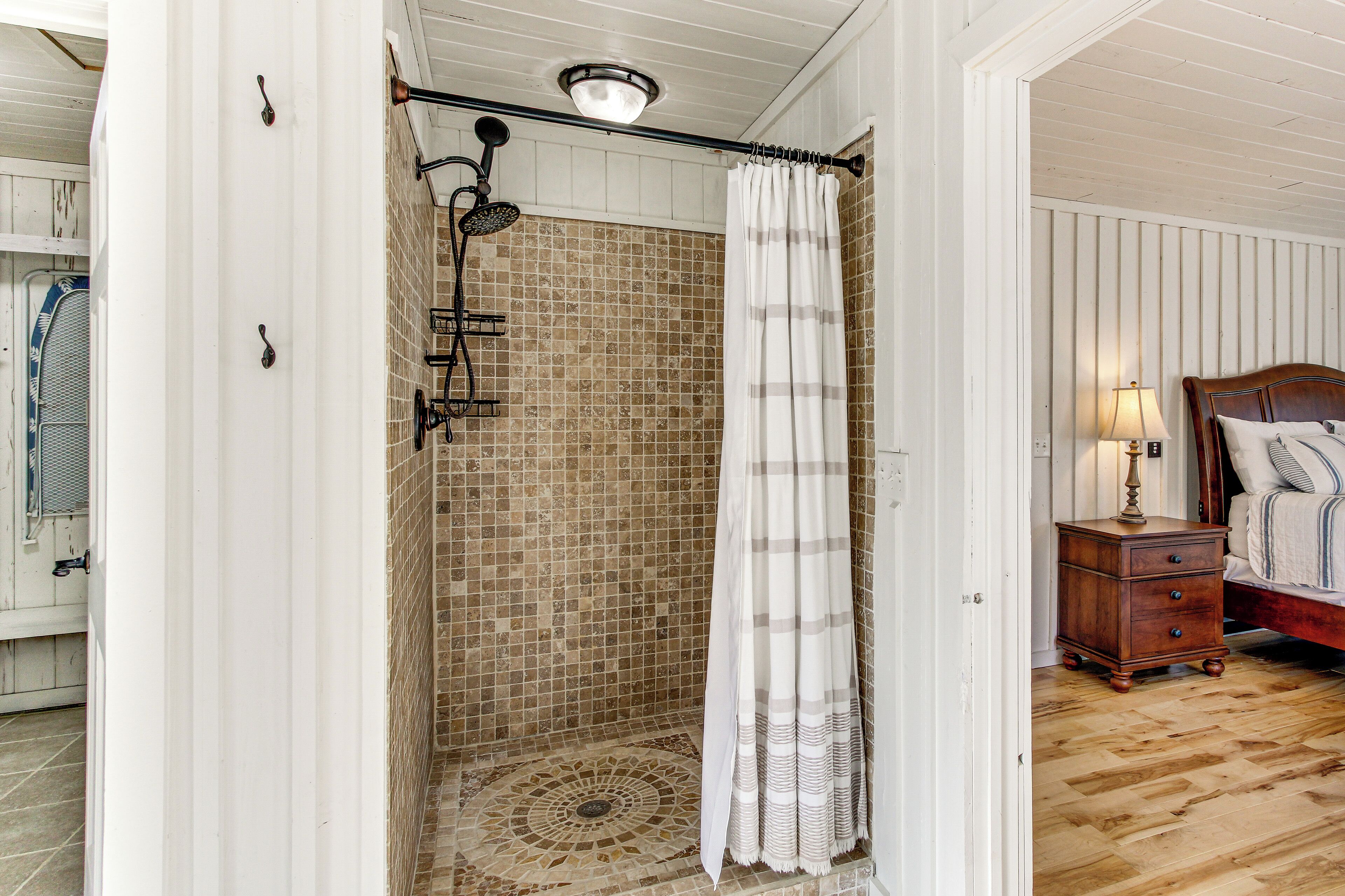 Une douche avec un mur carrelé, un plancher en bois, une table de chevet avec une lampe et un lit avec une tête de lit.