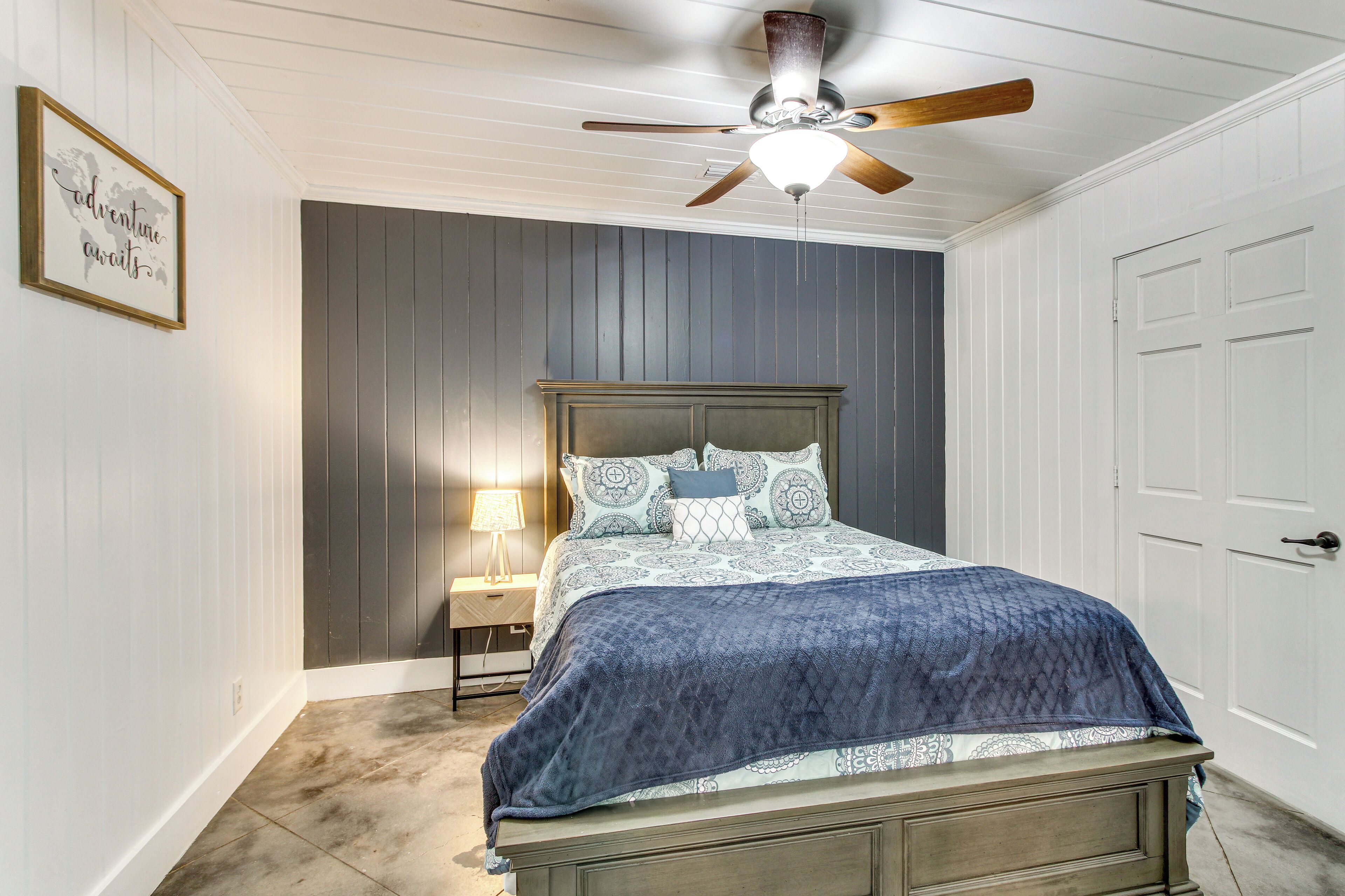 A bedroom with a bed, a ceiling fan, a nightstand, and a framed picture on the wall.