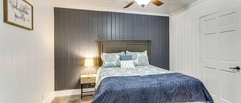 A bedroom with a bed, a ceiling fan, a nightstand, and a framed picture on the wall.