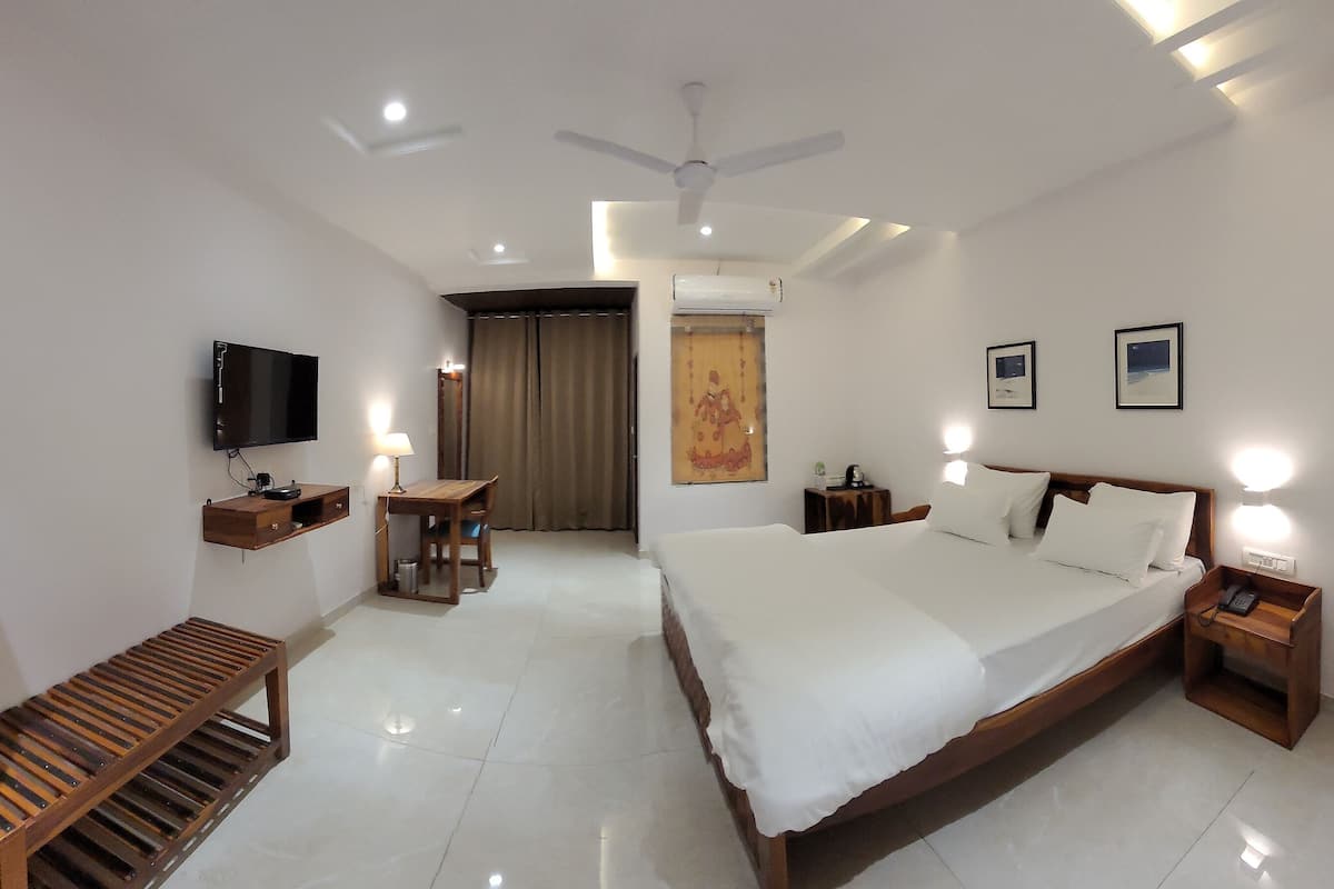 A hotel room with a large bed, bedside tables, a desk, a chair, a TV, and a ceiling fan.