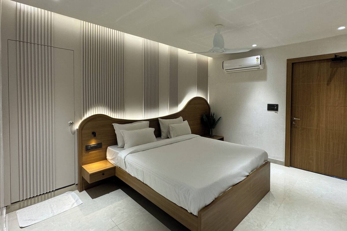 A modern bedroom with a wooden bed, a nightstand, a wall-mounted air conditioner, and a door.