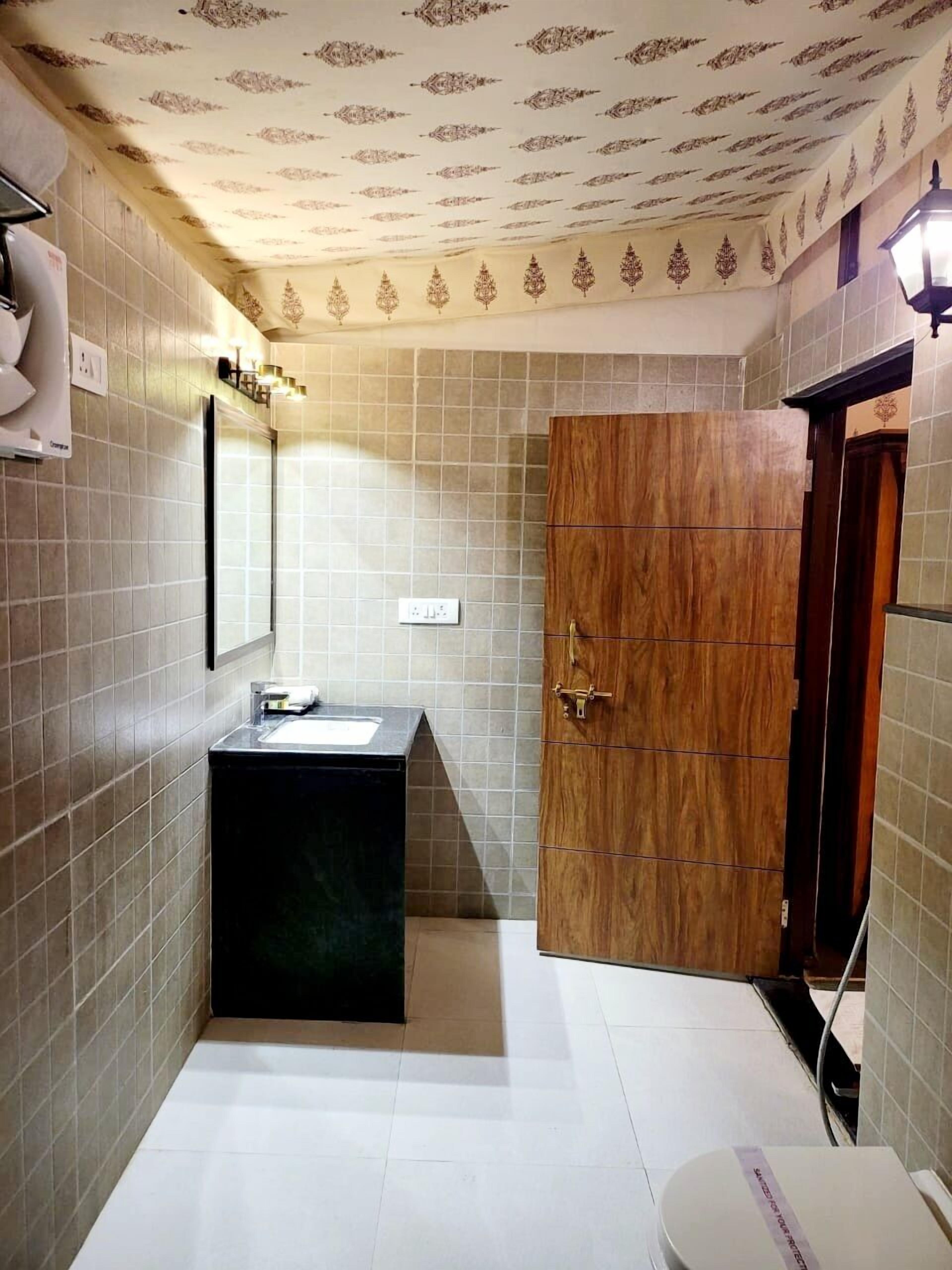 Un baño con suelo de baldosas, un armario de madera, un lavabo con espejo y una lámpara sobre el espejo.