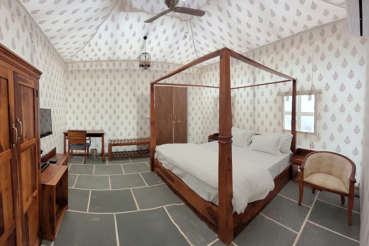 A four-poster bed with a wooden frame, a television on a wooden stand, a wooden wardrobe, and a patterned wallpaper.
