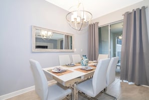 A dining area with a table, chairs, a chandelier, a mirror, and a vase.