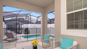 A covered outdoor seating area with a pool, white furniture, and a view of a house in the background. - Luxurious 4BR Home Pool Near Disney Storey Lake (Kissimmee)