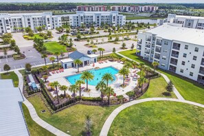 A modern hotel with a central pool, surrounded by palm trees and a well-maintained lawn.