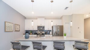 A modern kitchen with white cabinets, stainless steel appliances, and a central island with bar stools. - Luxurious 4BR Home Pool Near Disney Storey Lake (Kissimmee)