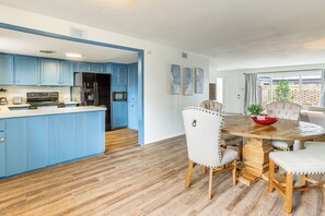 Una cocina moderna con armarios azules, una mesa de comedor de madera con sillas tapizadas de blanco y una isla grande con un fregadero.