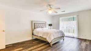 A bedroom with a bed, wooden flooring, a ceiling fan, and a window with blinds.