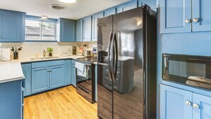 A kitchen with blue cabinets, a stainless steel refrigerator, a microwave, and a wooden floor.
