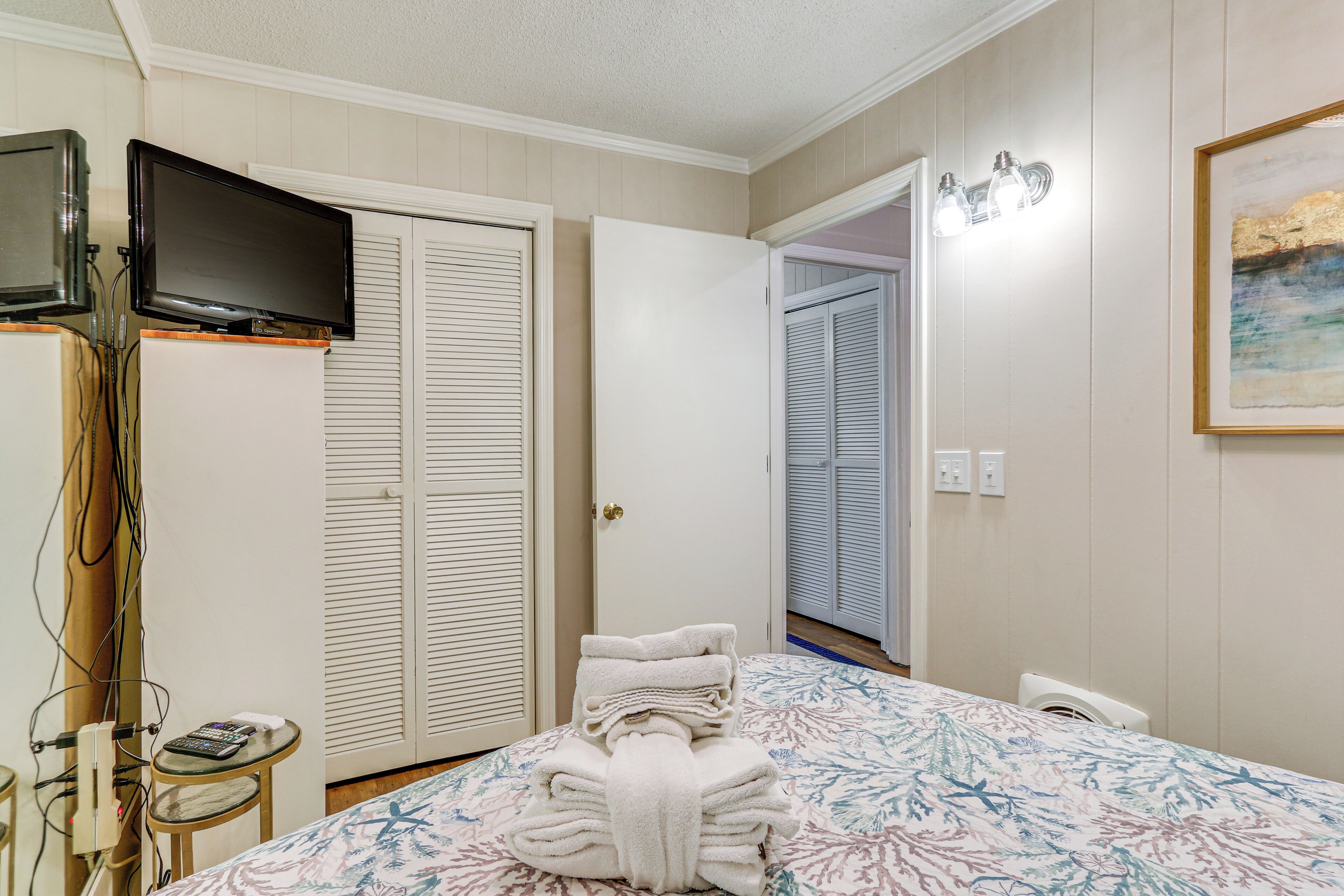 A hotel room with a bed, a television on a stand, a small table with a remote control, and a stack of towels.