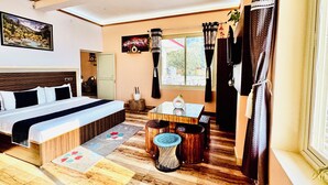Een hotelkamer met een bed, een klein tafeltje, een stoel, een raam met gordijnen en uitzicht op de omgeving.