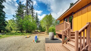 A wooden deck with a staircase leading to a yellow building, surrounded by trees and a gravel area. - Cle Elum Cabin on the Yakima River! (Cle Elum)