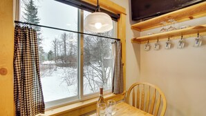 A wooden table with two wine glasses and a bottle, a window with checkered curtains, and a shelf with cups. - Cle Elum Cabin on the Yakima River! (Cle Elum)