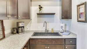 A kitchen with dark wooden cabinets, a granite countertop, a stainless steel sink, a coffee maker, and a vase with dried flowers on a shelf above the sink. - Private Oro Valley Home w/ 130 Mi Bike Path Nearby (Oro Valley)