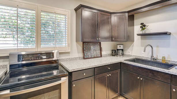 A kitchen with dark wooden cabinets, a stainless steel stove, a granite countertop, a double sink, and a window with blinds. - Private Oro Valley Home w/ 130 Mi Bike Path Nearby (Oro Valley)