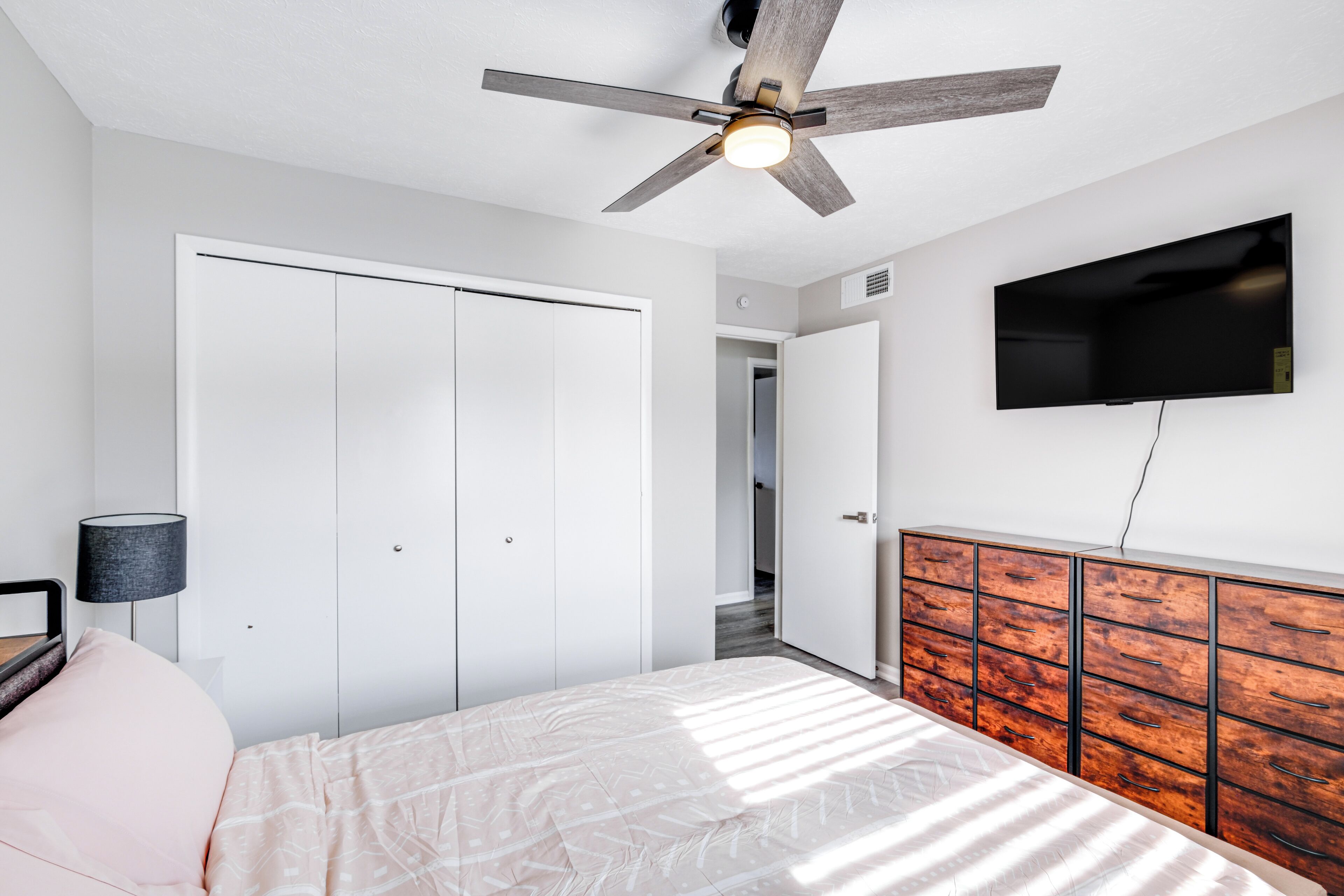 Une chambre à coucher comprenant un lit, un ventilateur de plafond, une télévision, une armoire et une lampe de chevet.
