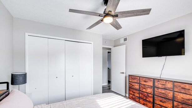 A bedroom with a bed, a ceiling fan, a TV, a wardrobe, and a bedside lamp.