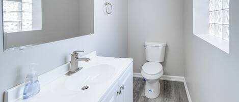 Un baño con lavamanos, espejo y retrete blancos.